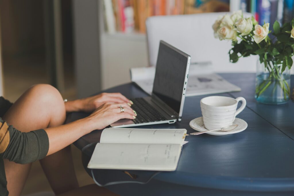Hands typing on a laptop with a notebook and cup on a table